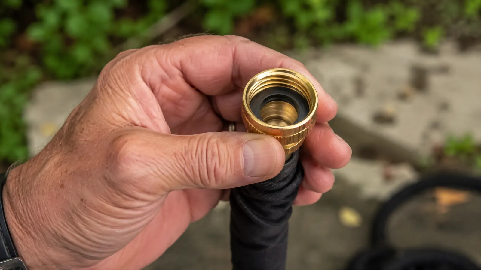 Close-up of an older man's hand checking the rubber washer inside the brass fitting of the Flexi Hose