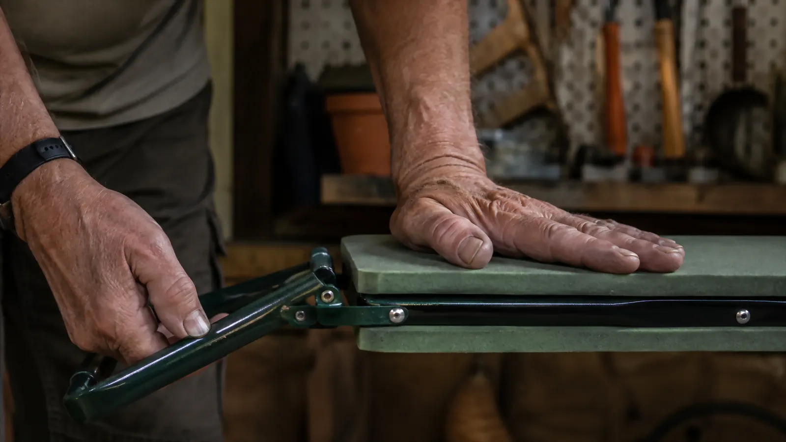 Close-up of hands folding the hinged steel frame of the KVR kneeler, thumb positioned carefully near the hinge