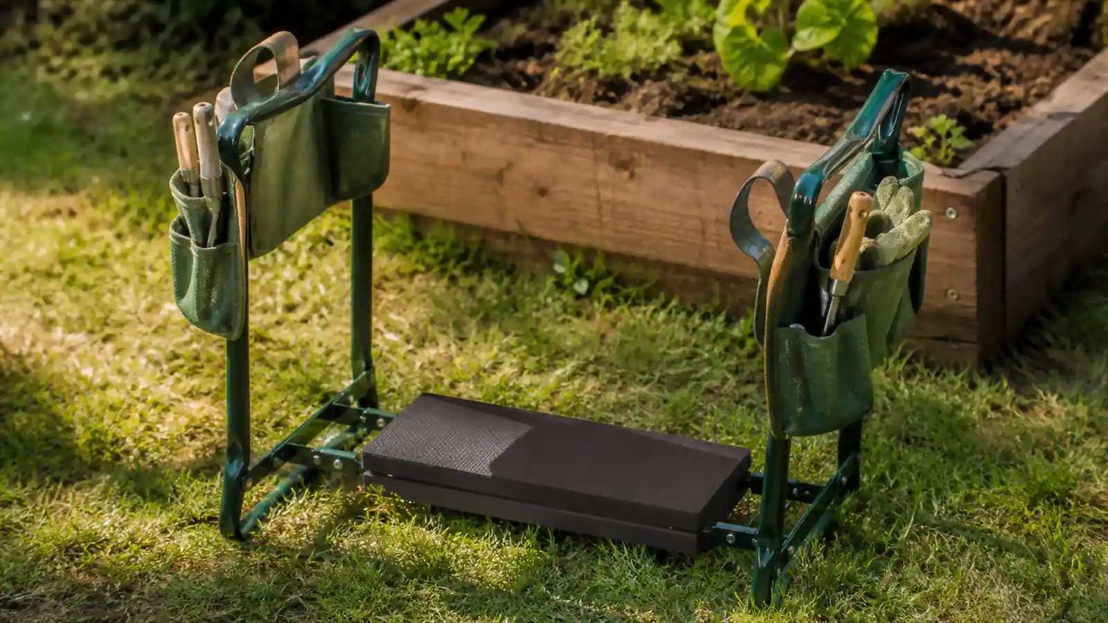 Close-up of a folding garden kneeler and seat with side tool pouches sitting beside a raised bed